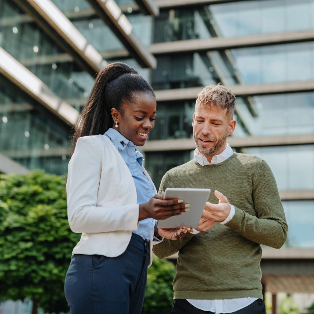 Zwei Asset-Management-Profis diskutieren ESG-Richtlinien auf einem Tablet vor einem modernen Bürogebäude